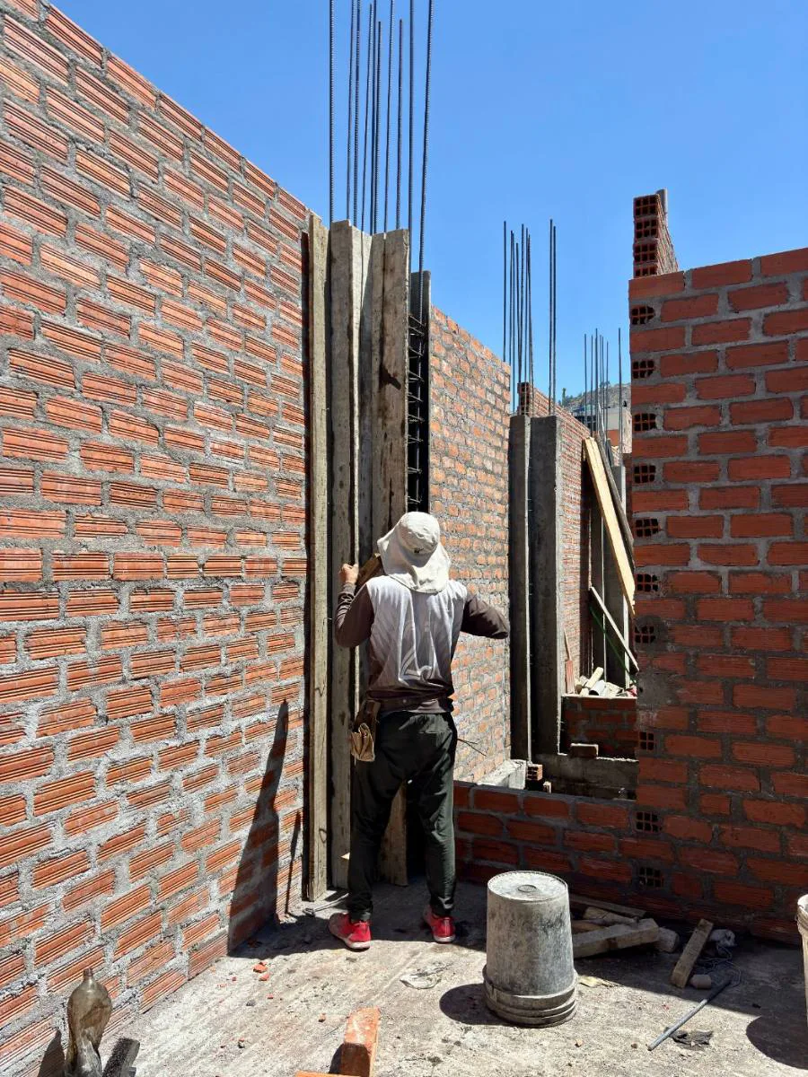 Operario levantando muro de ladrillo desde andamio